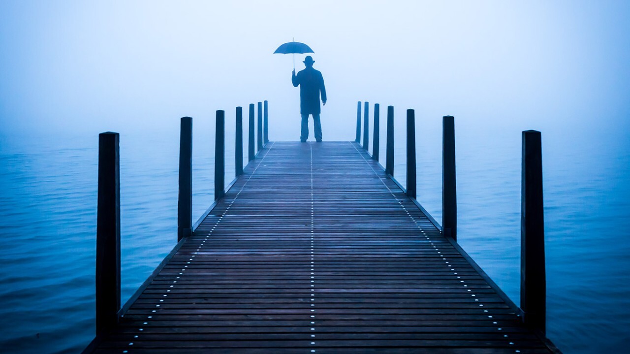 A man standing on a dock with an umbrella bids farewell.